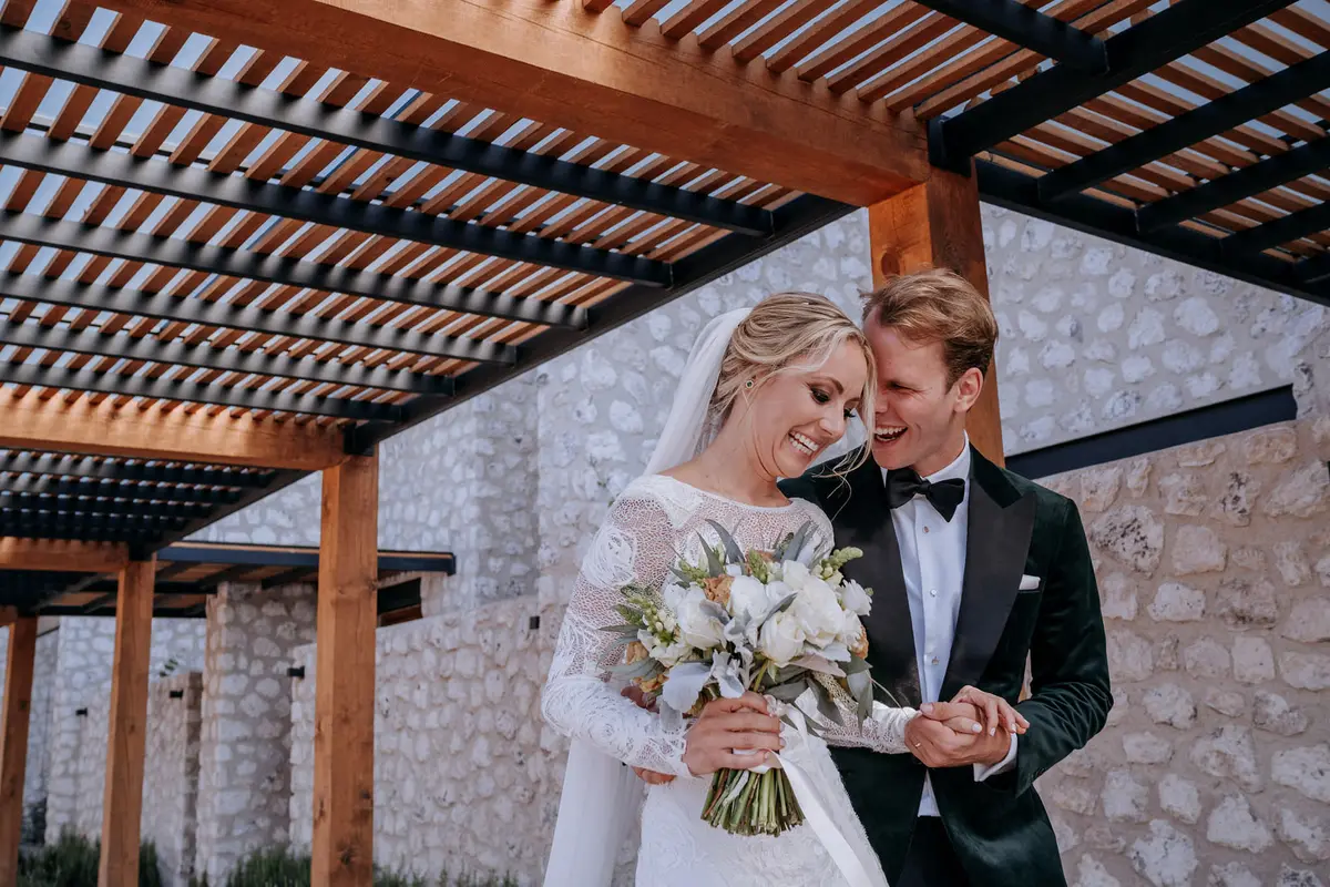 Newlyweds walking and laughing under a stone pergola in San Miguel de Allende
