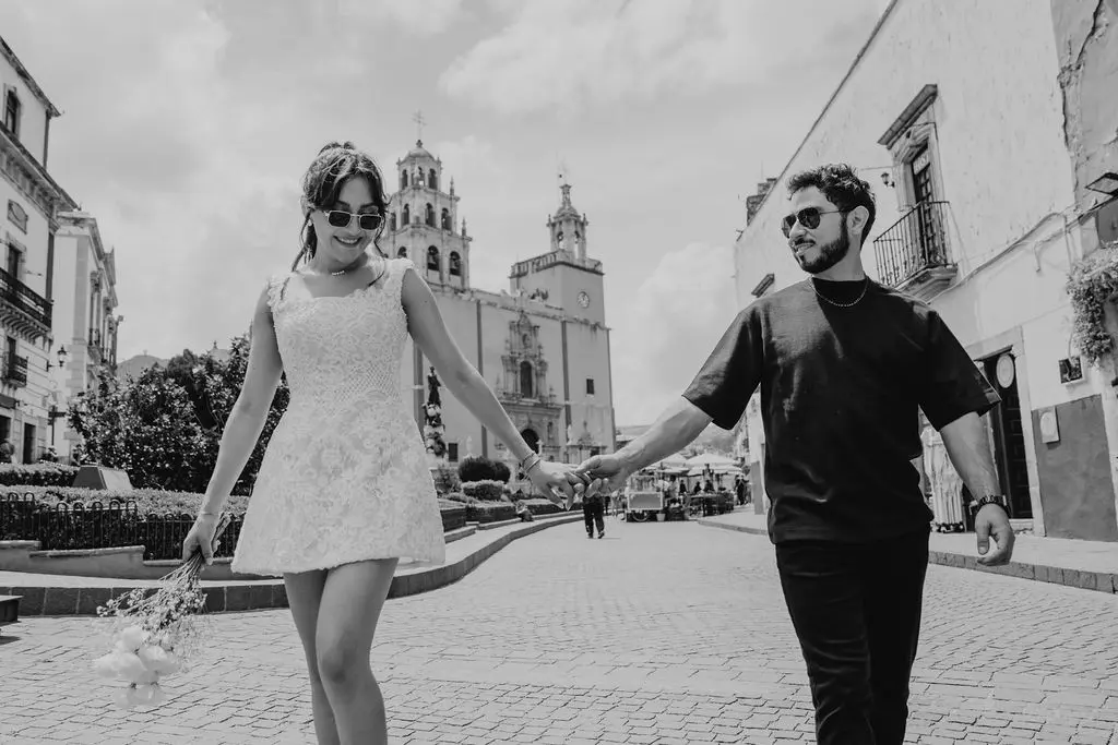 Black and white of the couple walking hand in hand near the yellow Basilica of Guanajuato.
