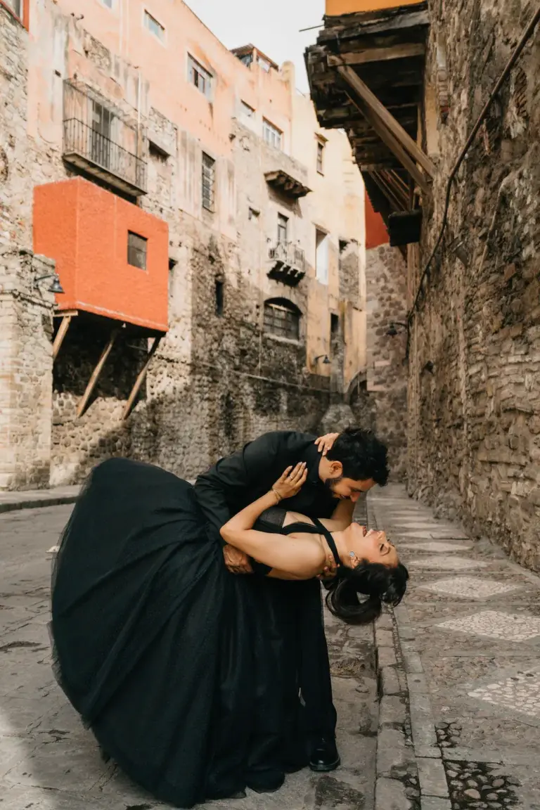 Dramatic dip kiss beneath bright orange balconies in a historic Guanajuato alleyway.