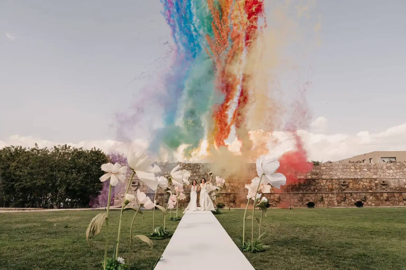 Two brides walking hand in hand with colorful smoke behind them at Hacienda Los Arcángeles, San Miguel de Allende