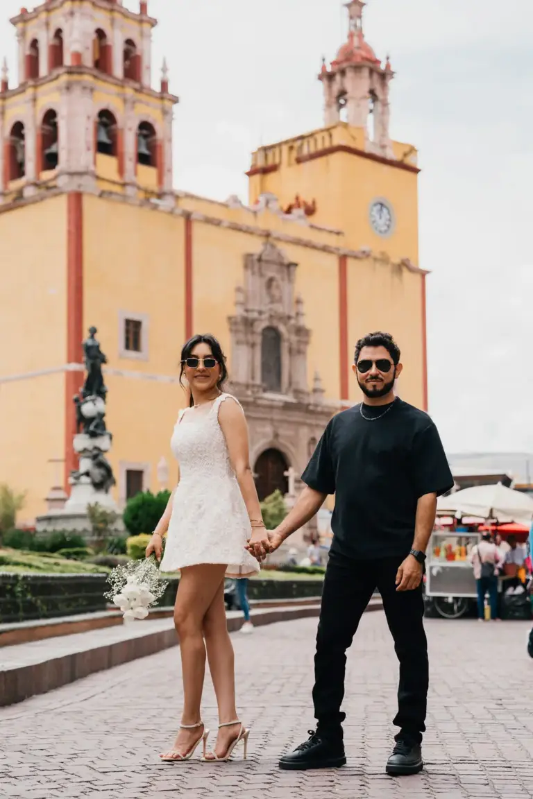 Pareja caminando hacia la cámara frente a la Basílica amarilla de Nuestra Señora de Guanajuato