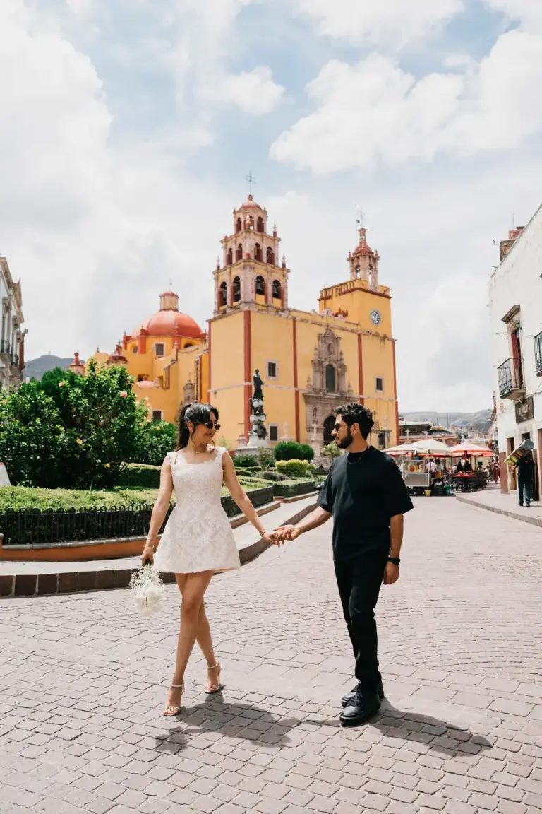 Pareja tomada de la mano frente a la Basílica amarilla de Guanajuato en su sesión de compromiso de destino