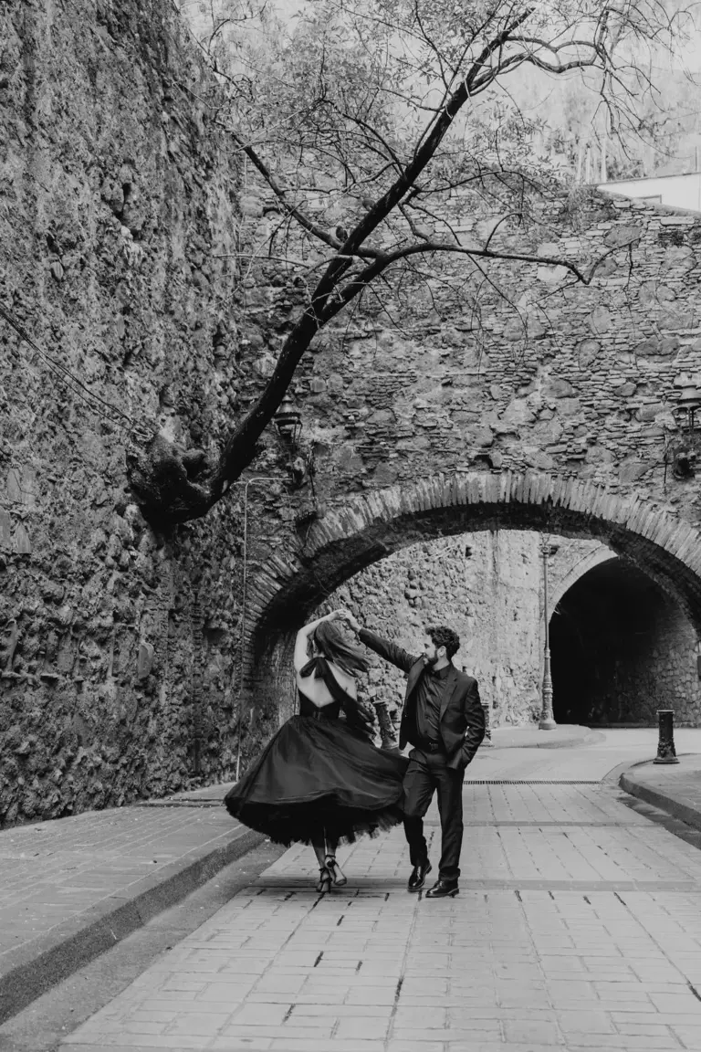Sesión de compromiso en Guanajuato, giro con vestido negro bajo un arco de piedra