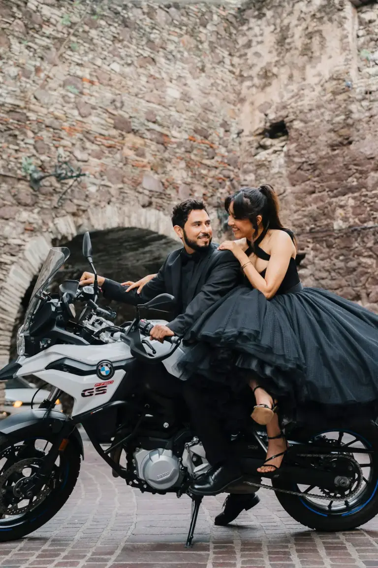 Pareja comprometida riendo sobre una motocicleta BMW GS, ella con un dramático vestido de tul negro, en Guanajuato