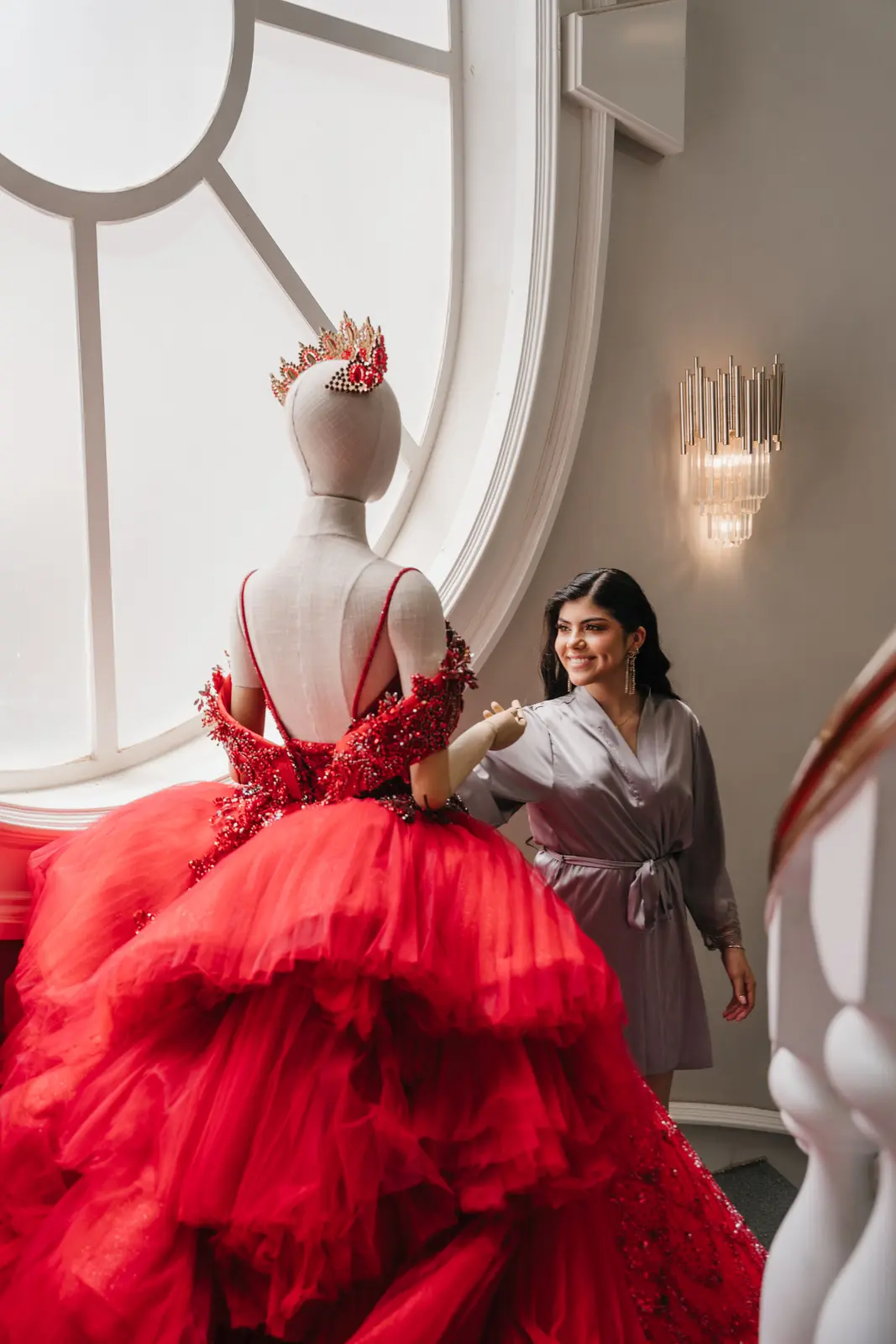 Quinceañera en bata junto a su vestido rojo de gala antes de vestirse