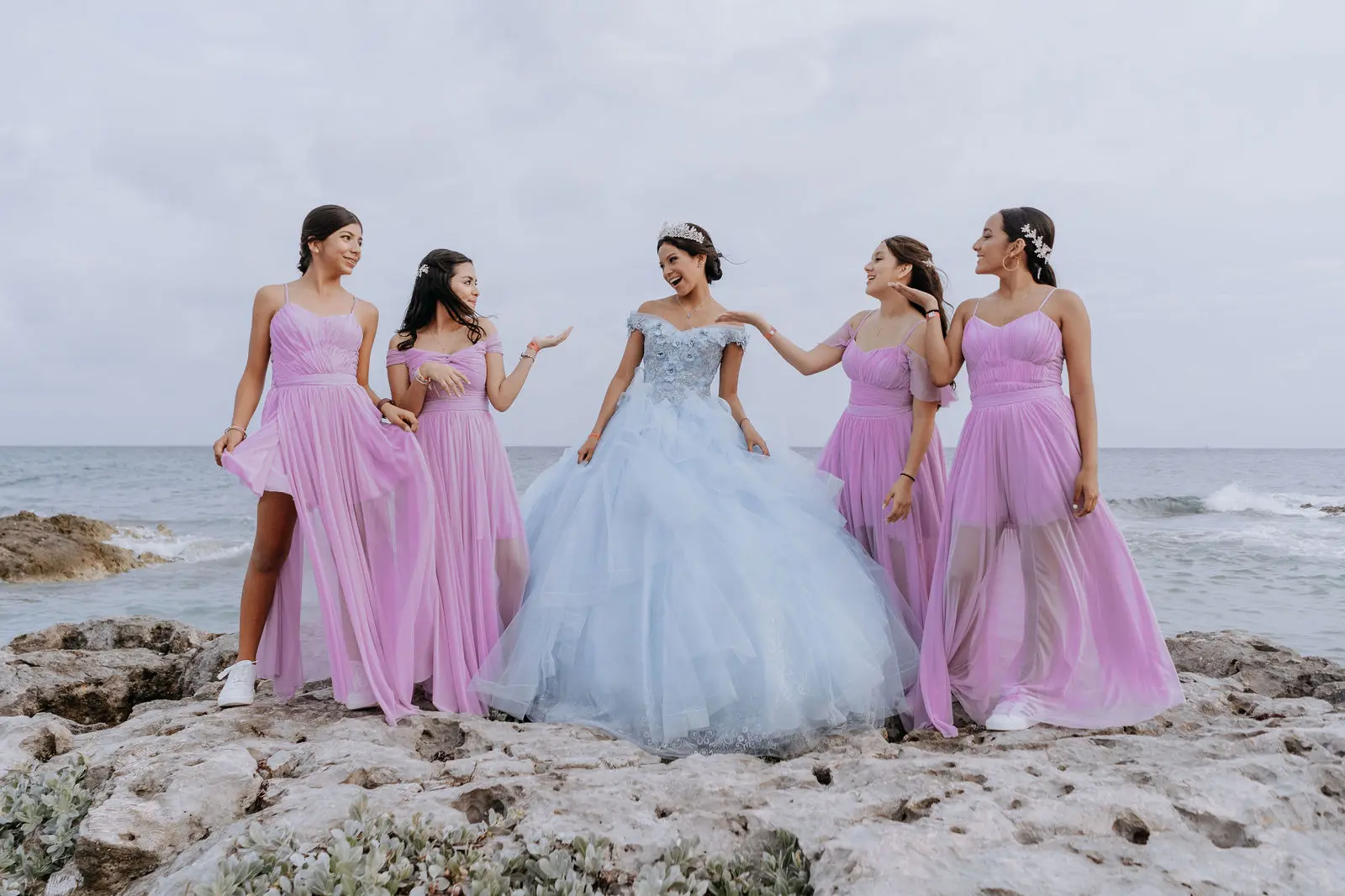 Quinceañera con vestido azul y damas en la playa