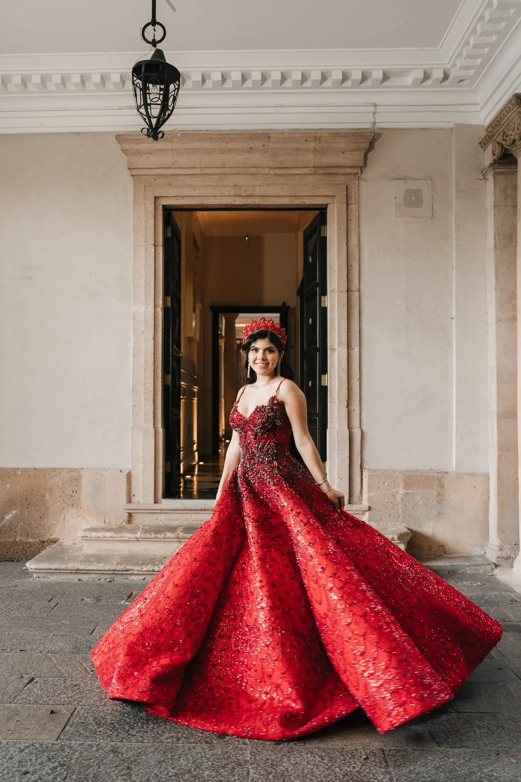 Quinceañera girando con vestido rojo bajo un arco de piedra
