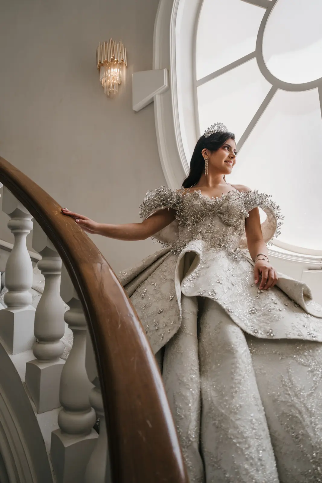 Quinceañera con vestido plateado apoyada en el barandal de una escalera